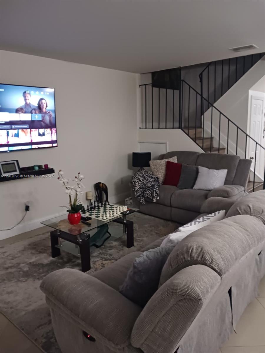 A living room features a wall-mounted television, gray sofas, a glass coffee table, and stairs — 8340 SW 154th Ave # 63, Miami FL 33193, MIAMI, FL