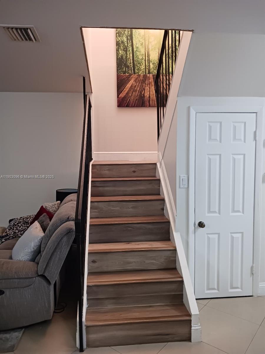 A staircase with wood-look treads leads upward next to a white door and sofa — 8340 SW 154th Ave # 63, Miami FL 33193, MIAMI, FL