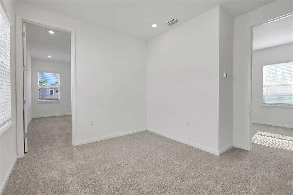 A carpeted room with white walls features two doorways leading to adjacent rooms with windows — 17125 STILLNESS ALLEY, WINTER GARDEN, FL