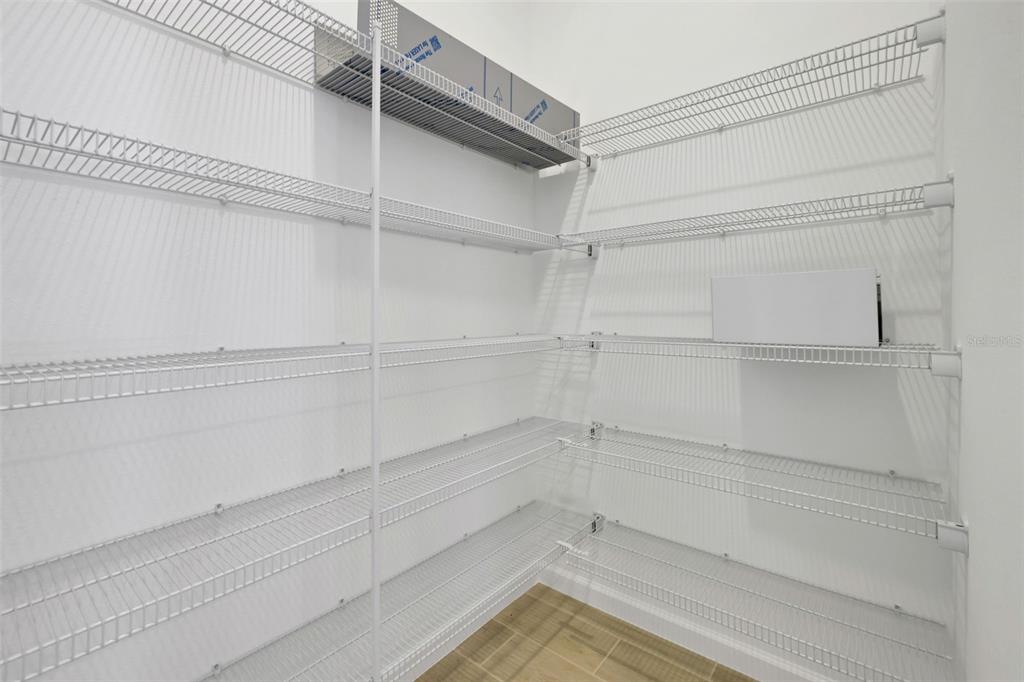 A walk-in pantry features white wire shelving units installed against plain white walls — 17125 STILLNESS ALLEY, WINTER GARDEN, FL