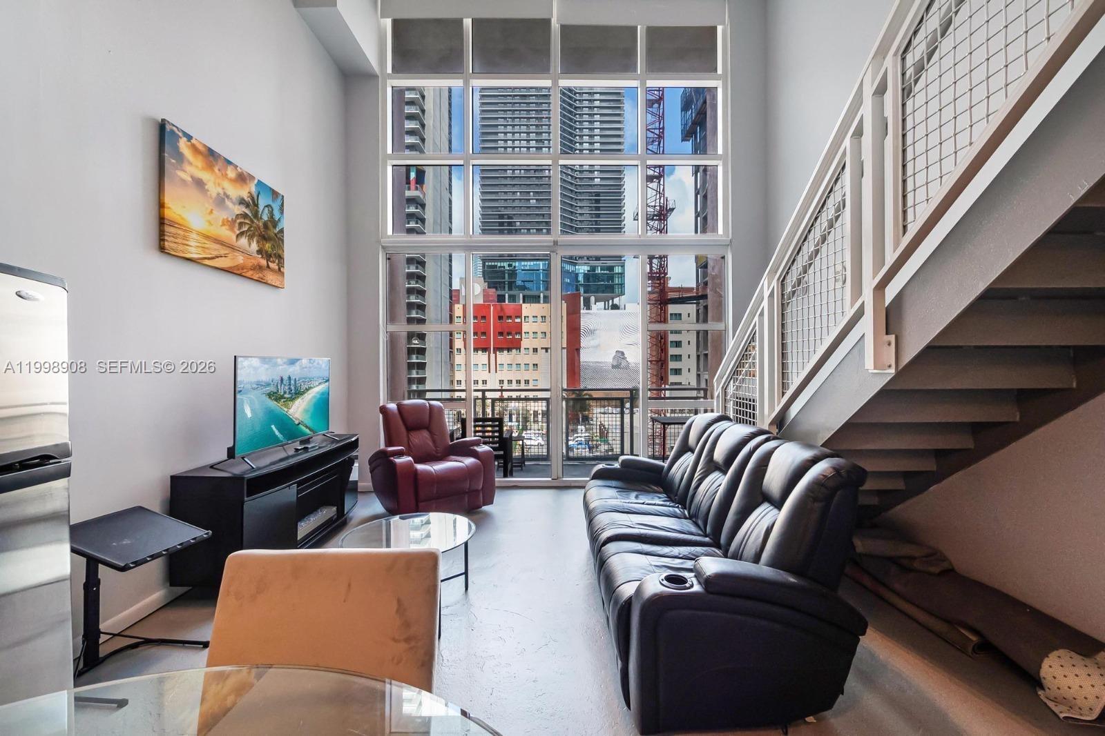 A living room features a tall window wall, a black leather sofa, and a staircase — 244 Biscayne Blvd # 445, Miami FL 33132, MIAMI, FL