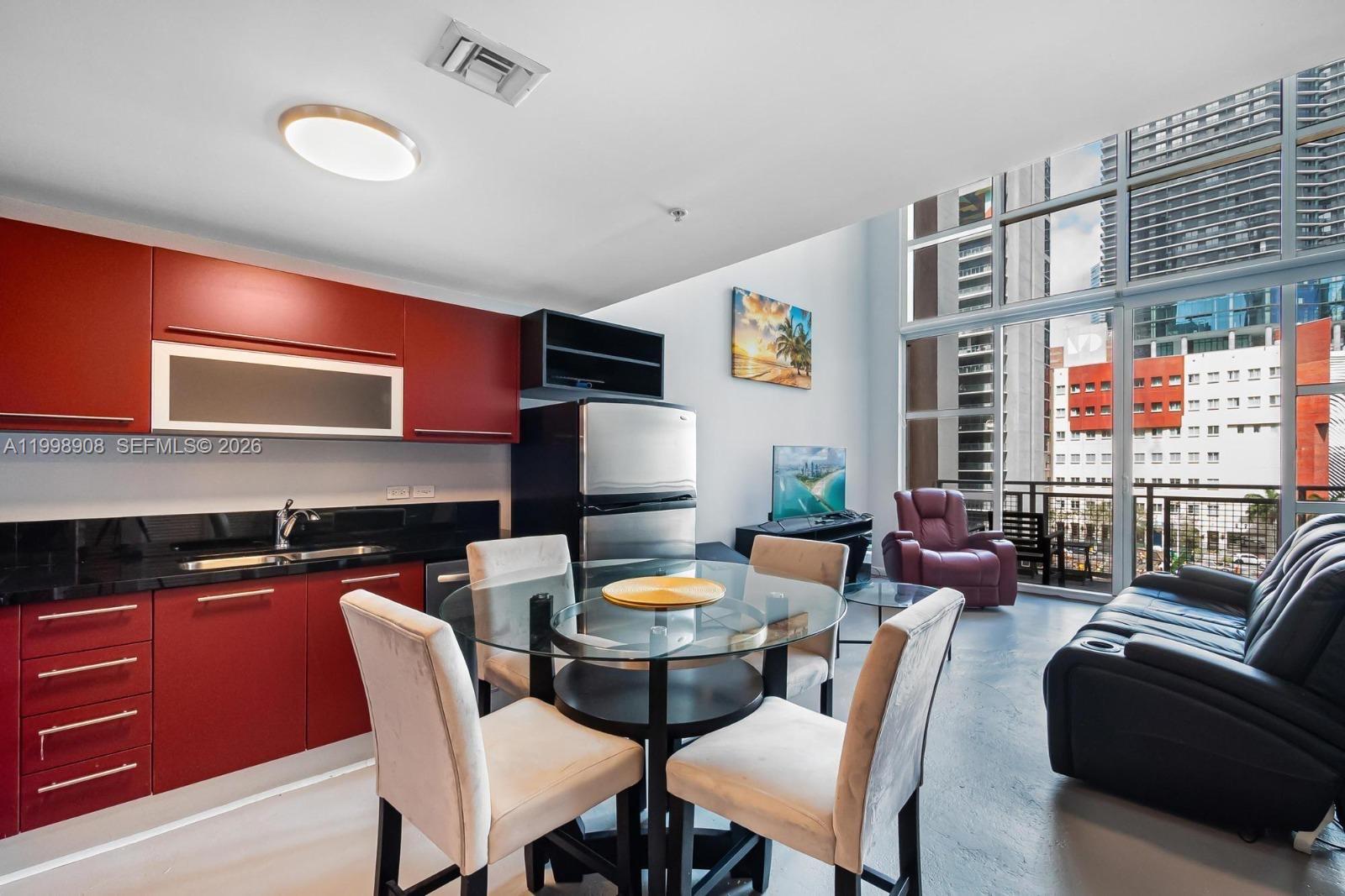 A kitchen and living area features red cabinetry, a glass dining table, and floor-to-ceiling windows — 244 Biscayne Blvd # 445, Miami FL 33132, MIAMI, FL