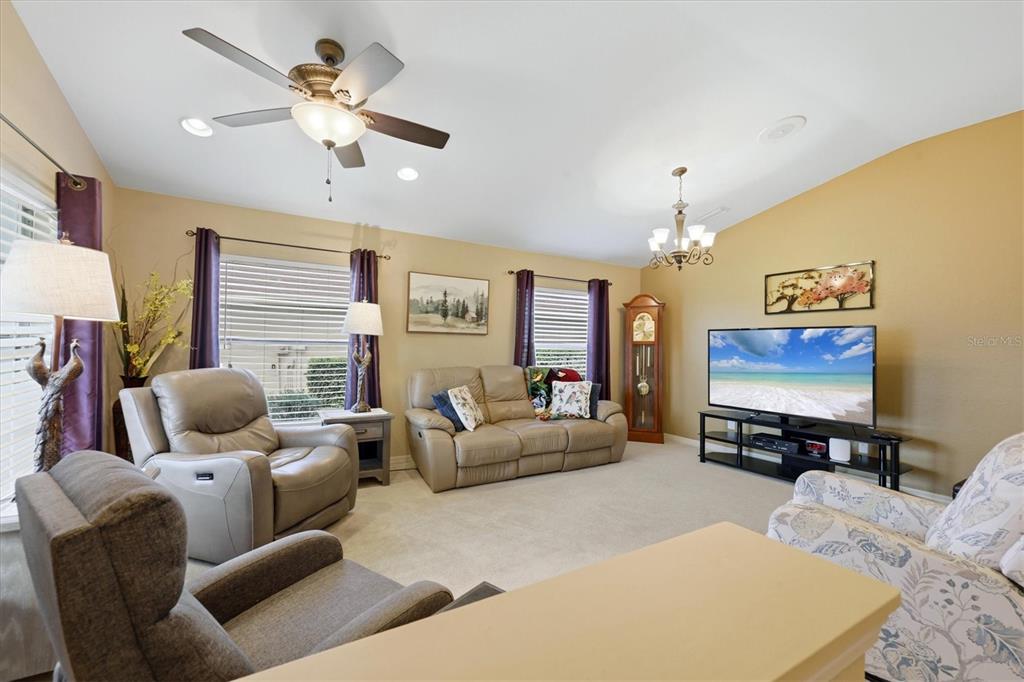 A living room features beige walls, carpeted flooring, a ceiling fan, and a television console — 1528 SCARLETT AVENUE, NORTH PORT, FL