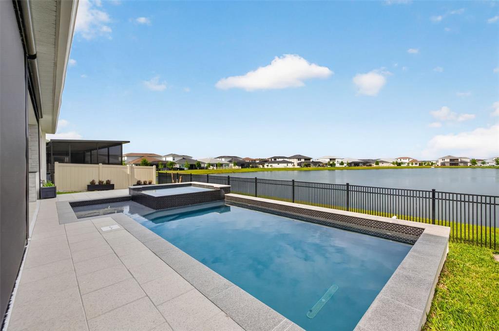 A rectangular swimming pool and raised spa overlook a lake behind a black metal fence — 8346 IVY STARK BOULEVARD, WESLEY CHAPEL, FL