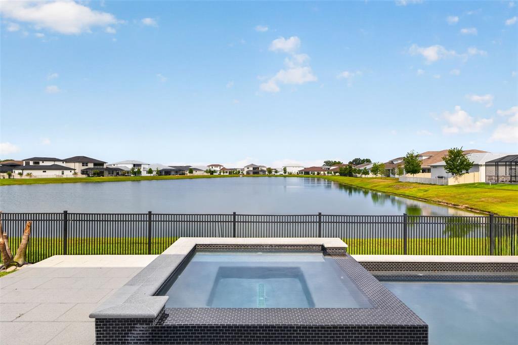 A backyard hot tub and pool overlook a lake surrounded by residential houses — 8346 IVY STARK BOULEVARD, WESLEY CHAPEL, FL