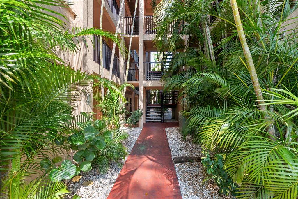 A red walkway leads through a tropical courtyard toward an outdoor staircase between apartment buildings — 3700 S OSPREY AVENUE UNIT 118, SARASOTA, FL