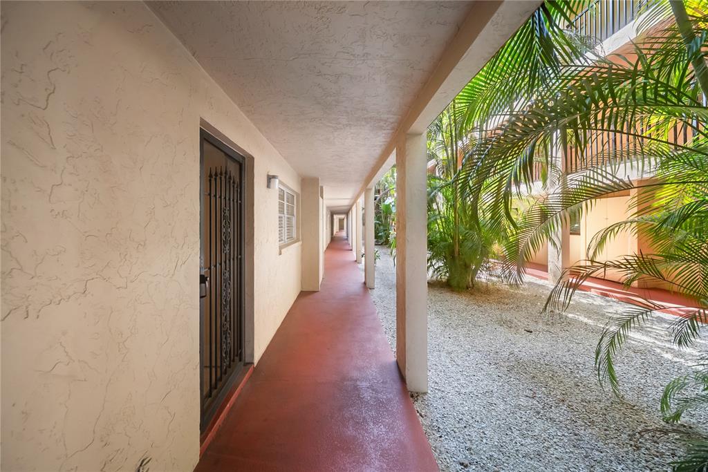 An outdoor covered walkway with a red floor leads past building entrances and palm trees — 3700 S OSPREY AVENUE UNIT 118, SARASOTA, FL
