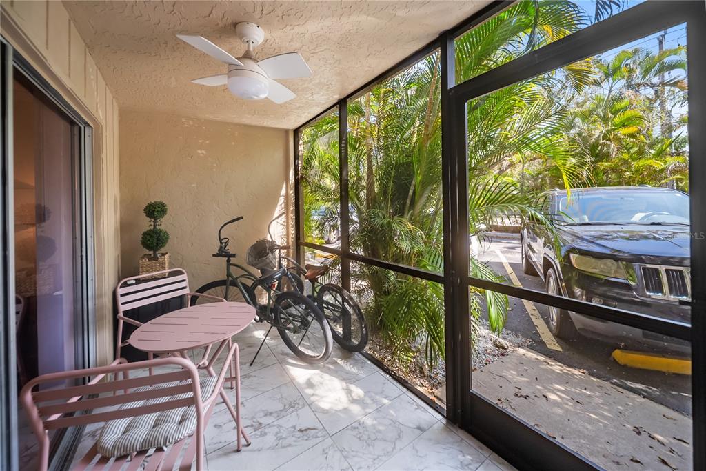 A screened-in patio features a pink metal bistro set, two bicycles, and tiled flooring — 3700 S OSPREY AVENUE UNIT 118, SARASOTA, FL