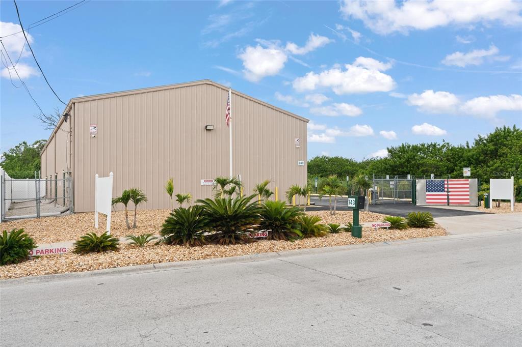 A tan metal warehouse building features a gravel landscape, palm plants, and a gated entrance — 743 WESLEY AVENUE, TARPON SPRINGS, FL