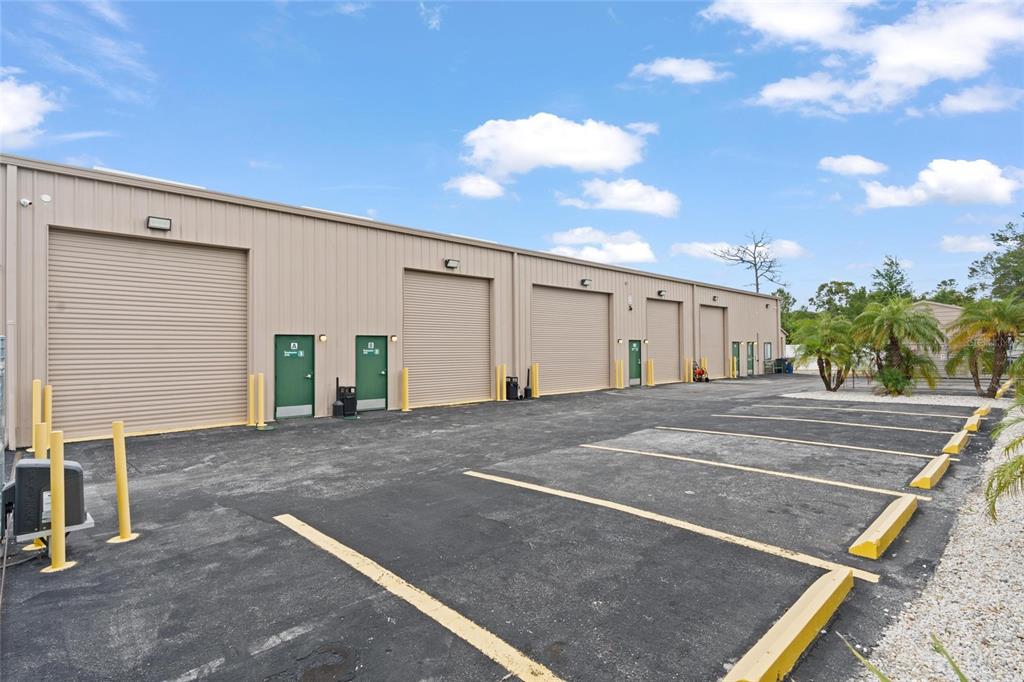A row of industrial warehouse units with roll-up doors and green entry doors — 743 WESLEY AVENUE, TARPON SPRINGS, FL