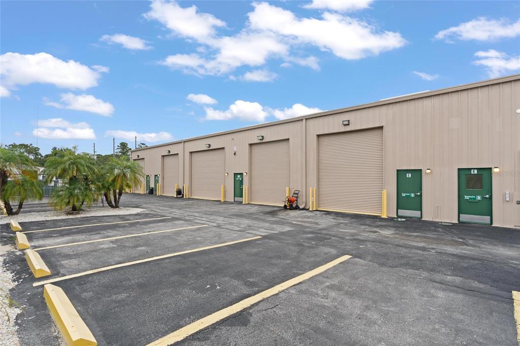 An exterior view of a commercial warehouse building with multiple roll-up doors and green entrances — 743 WESLEY AVENUE, TARPON SPRINGS, FL