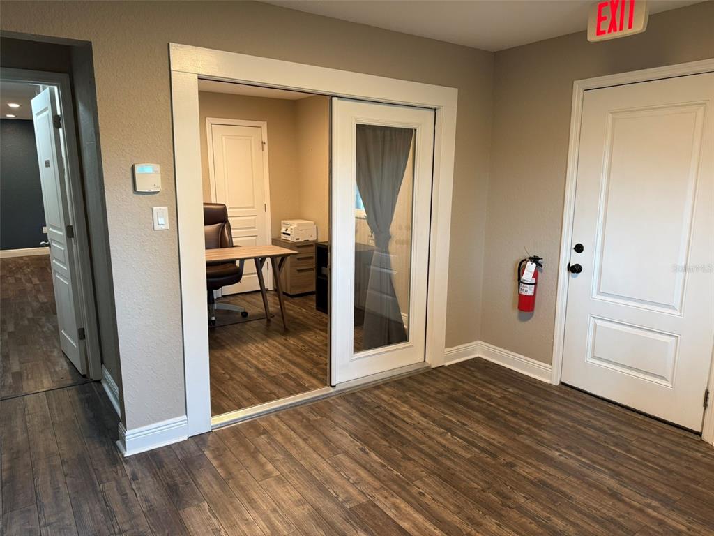 A room with wood-look flooring features a glass-paneled sliding door opening into an office space — 20785 W MCKINNEY AVENUE, DUNNELLON, FL