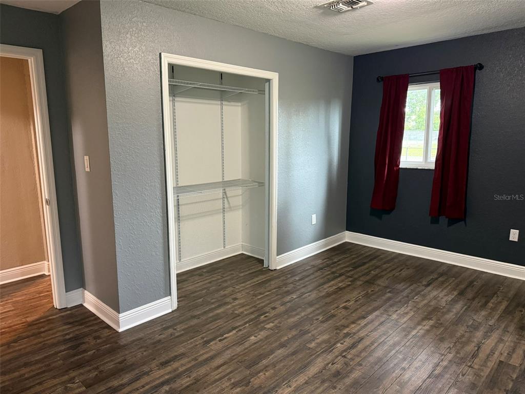 A bedroom features dark wood-look flooring, gray walls, a closet, and a window with curtains — 20785 W MCKINNEY AVENUE, DUNNELLON, FL