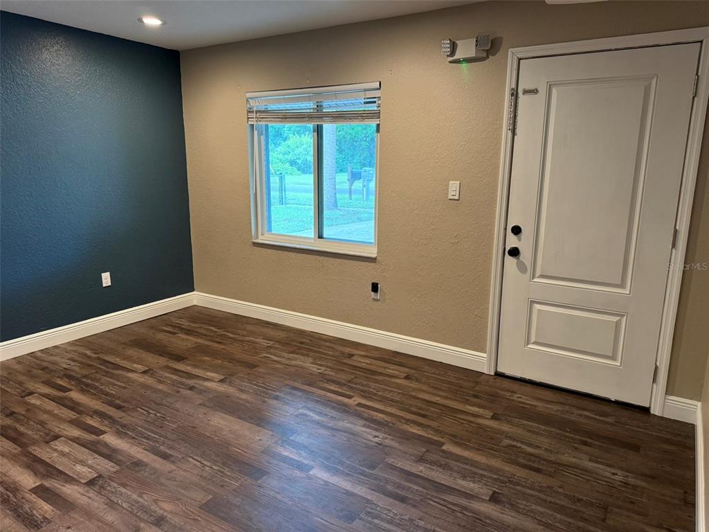 A room with dark wood-look flooring, a blue accent wall, a window, and a door — 20785 W MCKINNEY AVENUE, DUNNELLON, FL