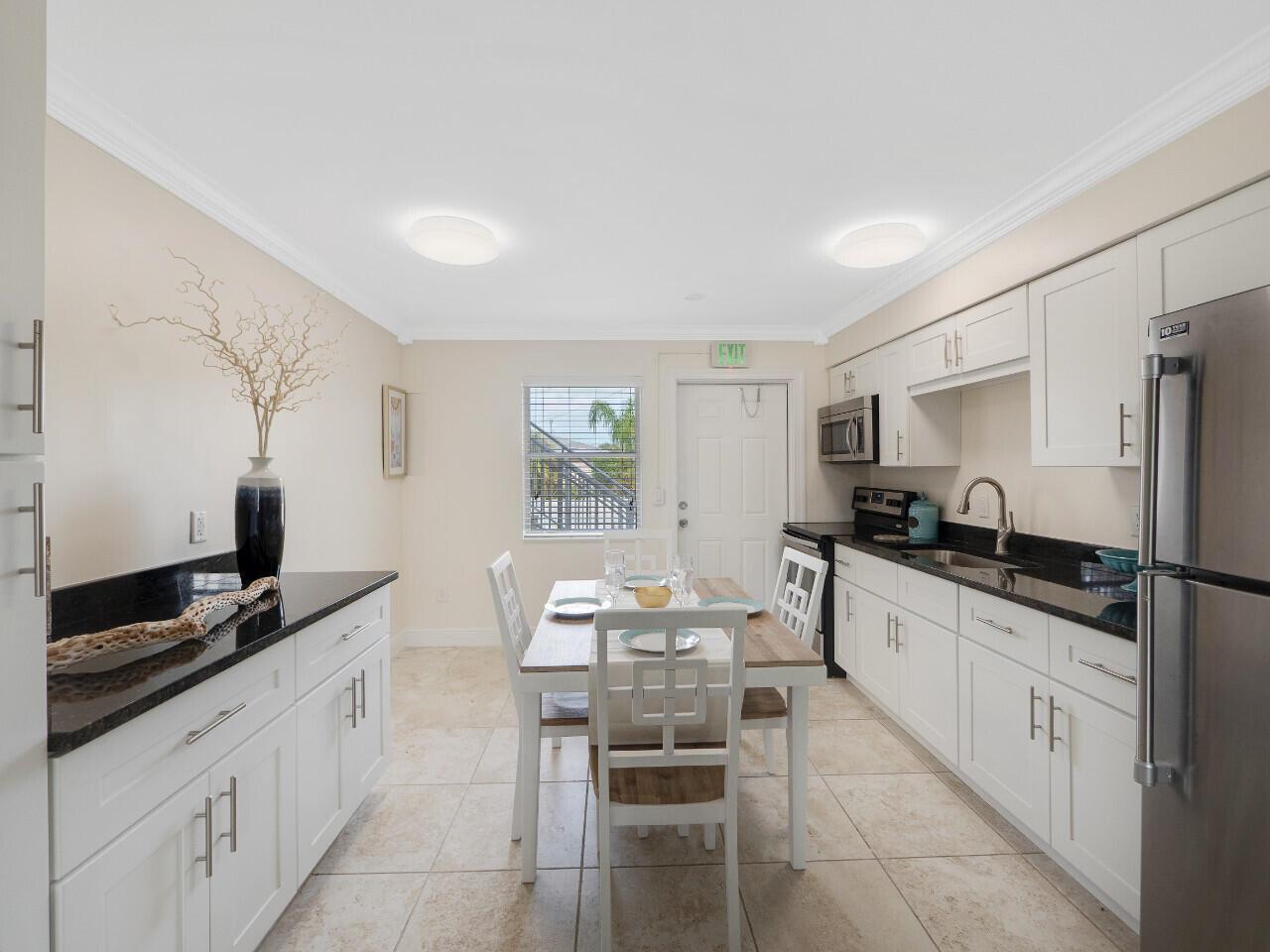 A kitchen and dining area with white cabinets, black countertops, and tile flooring — 1236 Beach Road # 2, Riviera Beach FL 33404, RIVIERA BEACH, FL