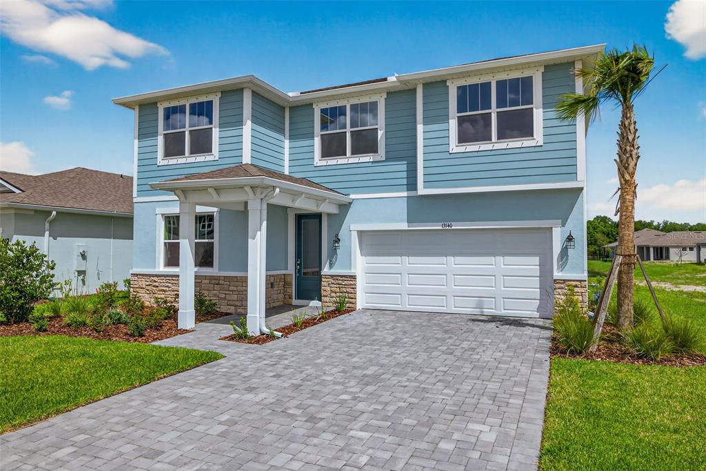 A two-story house with blue siding, a stone base, and a paved driveway — 13140 OXEYE LANE, PARRISH, FL