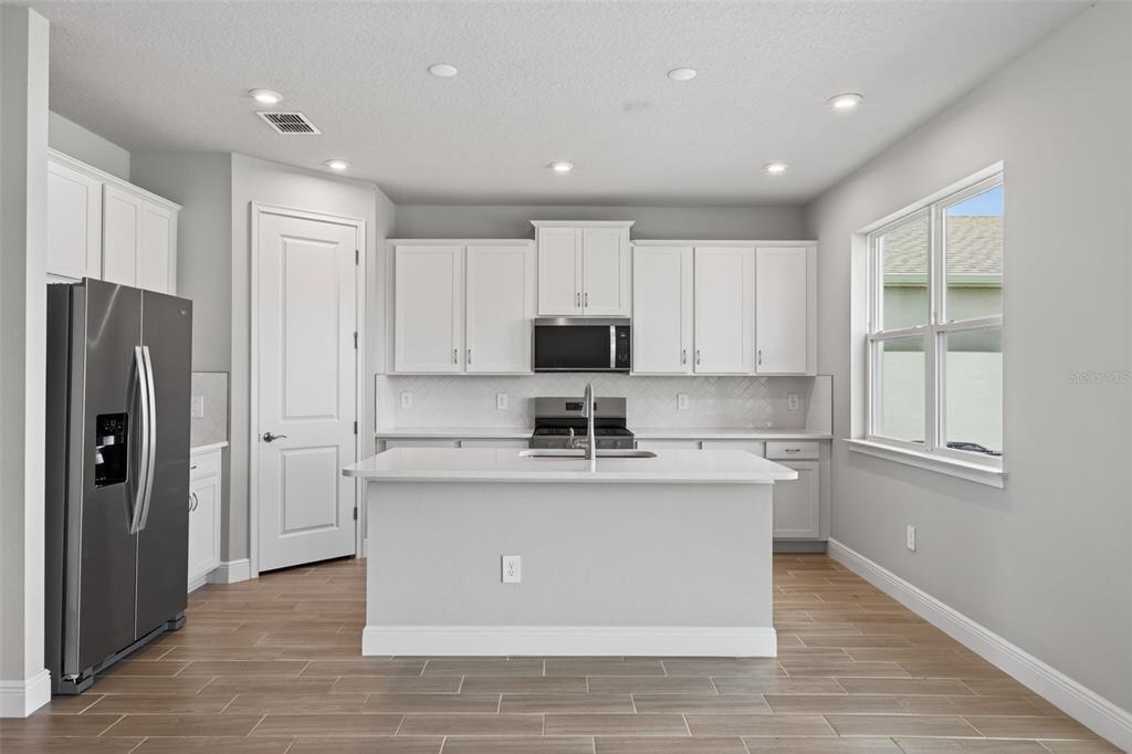 A modern kitchen features white cabinets, a central island, stainless steel appliances, and wood-look flooring — 13140 OXEYE LANE, PARRISH, FL