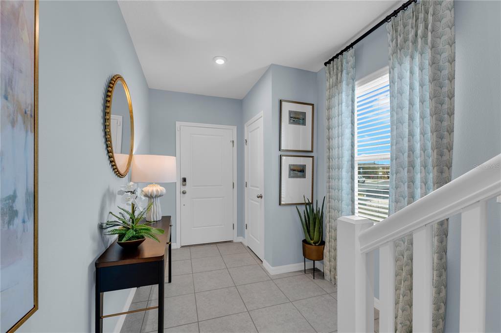 An entryway features light blue walls, tile flooring, a console table, and a staircase railing — 1908 FAN PALM DRIVE, DAVENPORT, FL