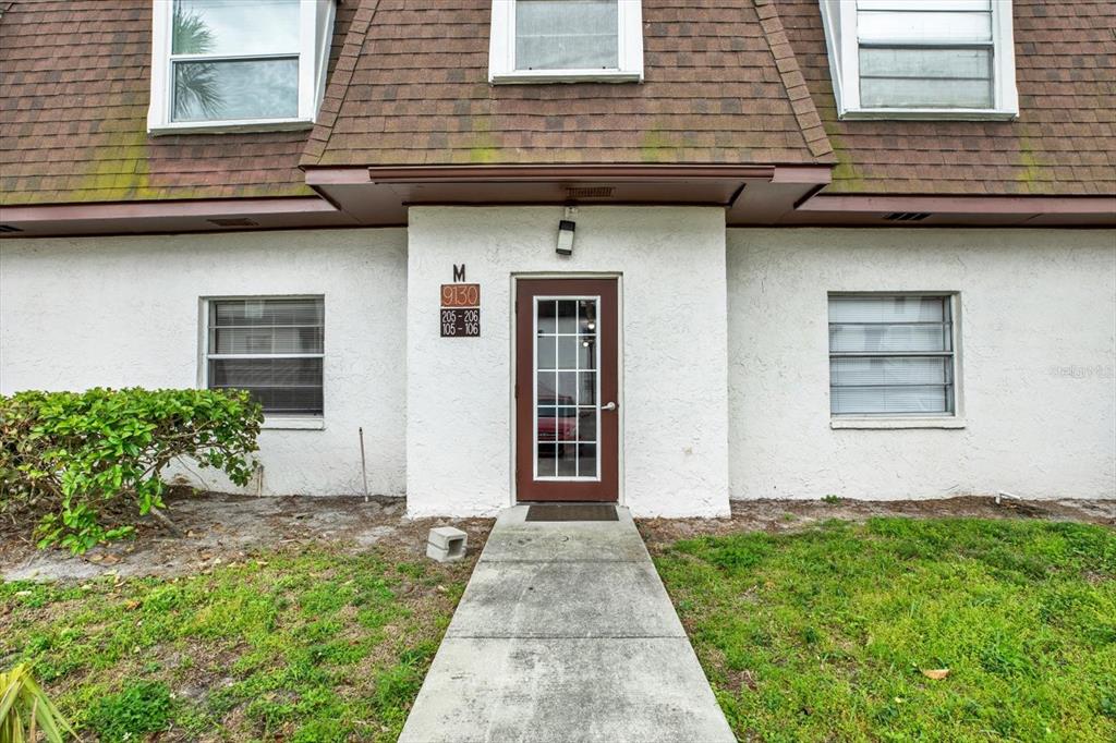 A brown-trimmed door and walkway lead to the entrance of a white stucco apartment building — 9130 TUDOR DRIVE UNIT M105, TAMPA, FL