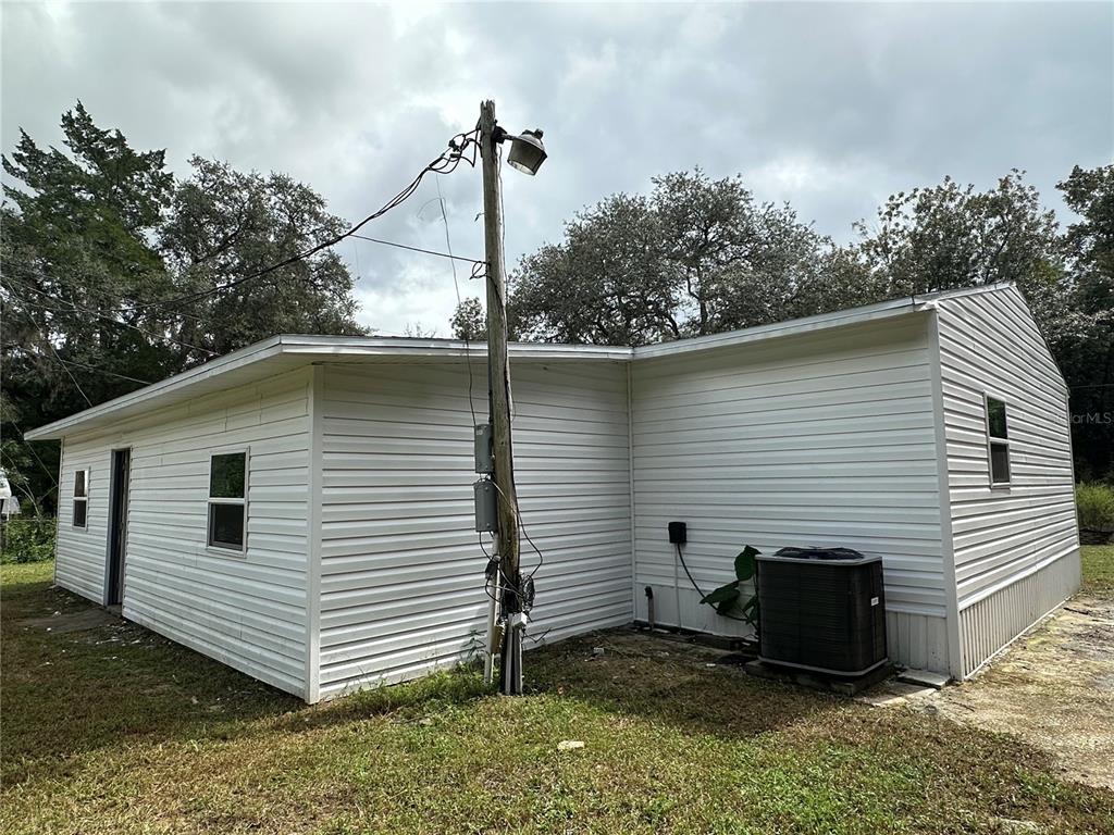 The exterior of a white, vinyl-sided house features a utility pole and an HVAC unit — 17405 NE 38TH LANE ROAD, SILVER SPRINGS, FL