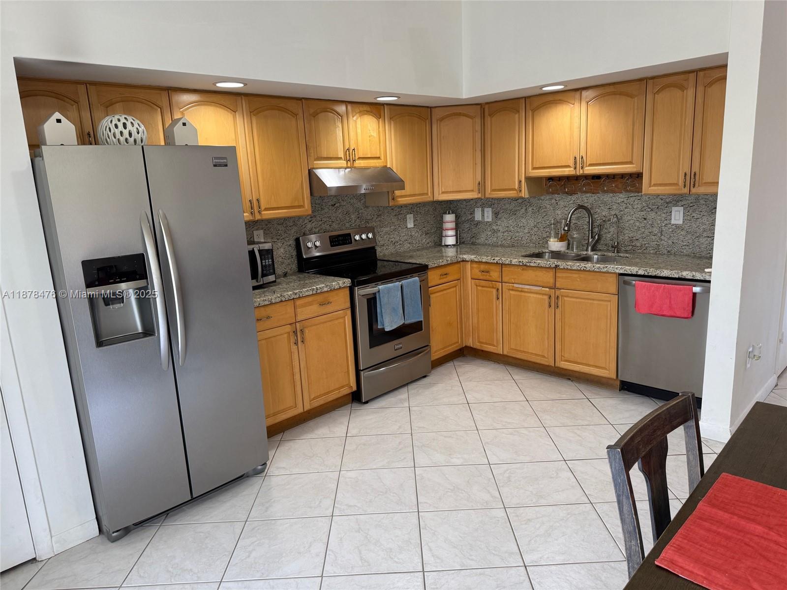 A kitchen features light wood cabinets, granite countertops, stainless steel appliances, and tiled flooring — 12413 SW 112th Ter, Miami FL 33186, MIAMI, FL