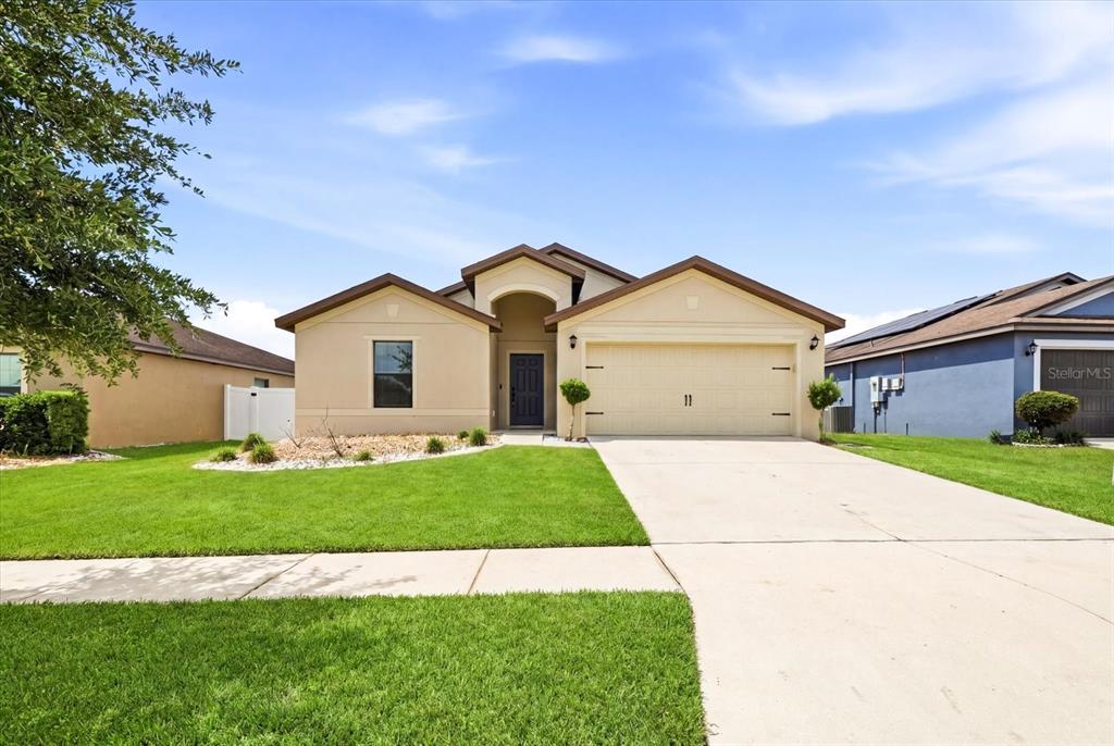 A single-story beige house with a two-car garage and a front lawn — 680 SWALLOWTAIL DRIVE, HAINES CITY, FL