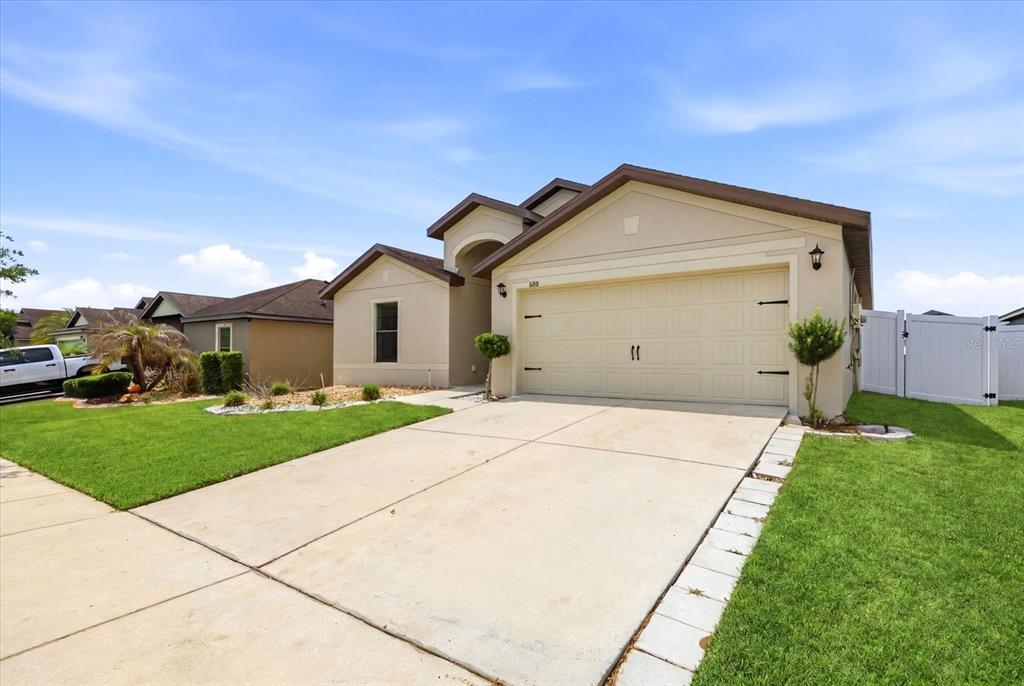 A single-story suburban house with a beige stucco exterior, two-car garage, and concrete driveway — 680 SWALLOWTAIL DRIVE, HAINES CITY, FL