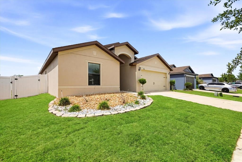 A tan single-story house with a two-car garage and a landscaped front yard — 680 SWALLOWTAIL DRIVE, HAINES CITY, FL