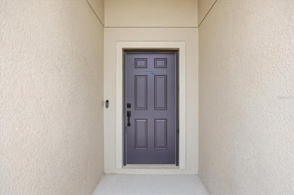 A dark gray front door with a recessed panel design is set within a beige entryway — 680 SWALLOWTAIL DRIVE, HAINES CITY, FL