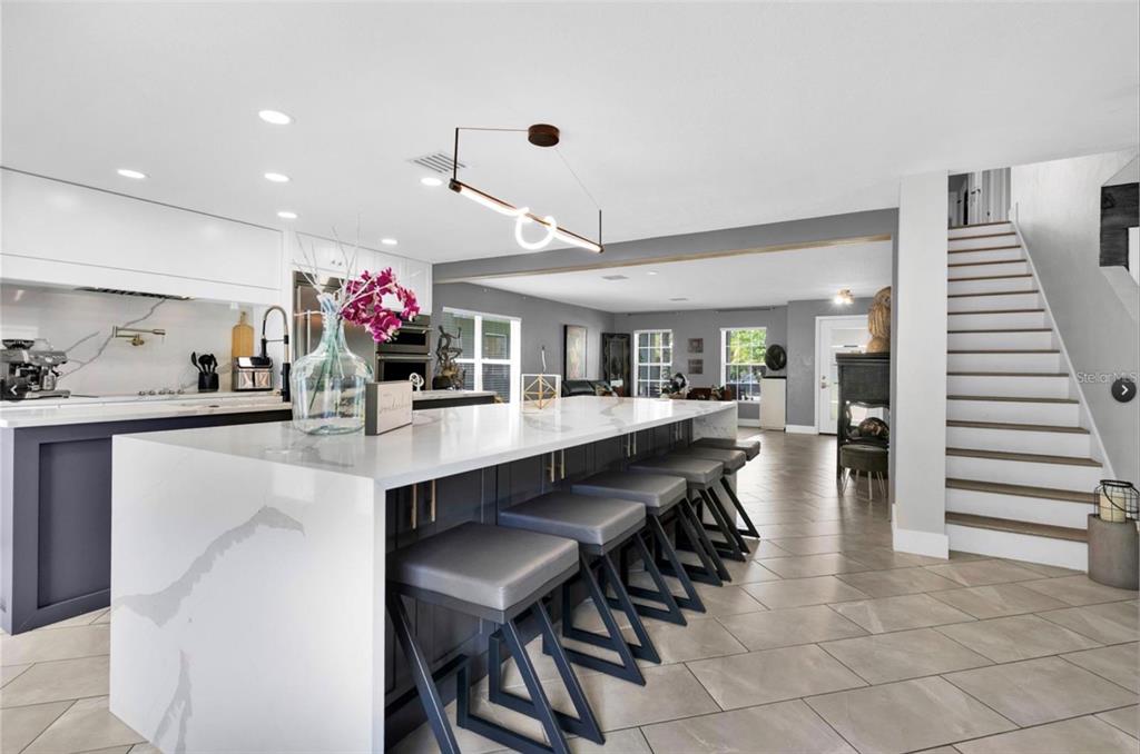 A modern kitchen features a large white waterfall island with grey stools and a staircase — 1652 ALGONKIN LOOP, ORLANDO, FL