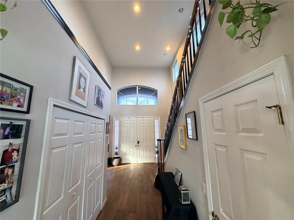 A high-ceilinged foyer features wood flooring, a staircase with a wooden railing, and double doors — 4165 COPPER HILL DRIVE, SPRING HILL, FL