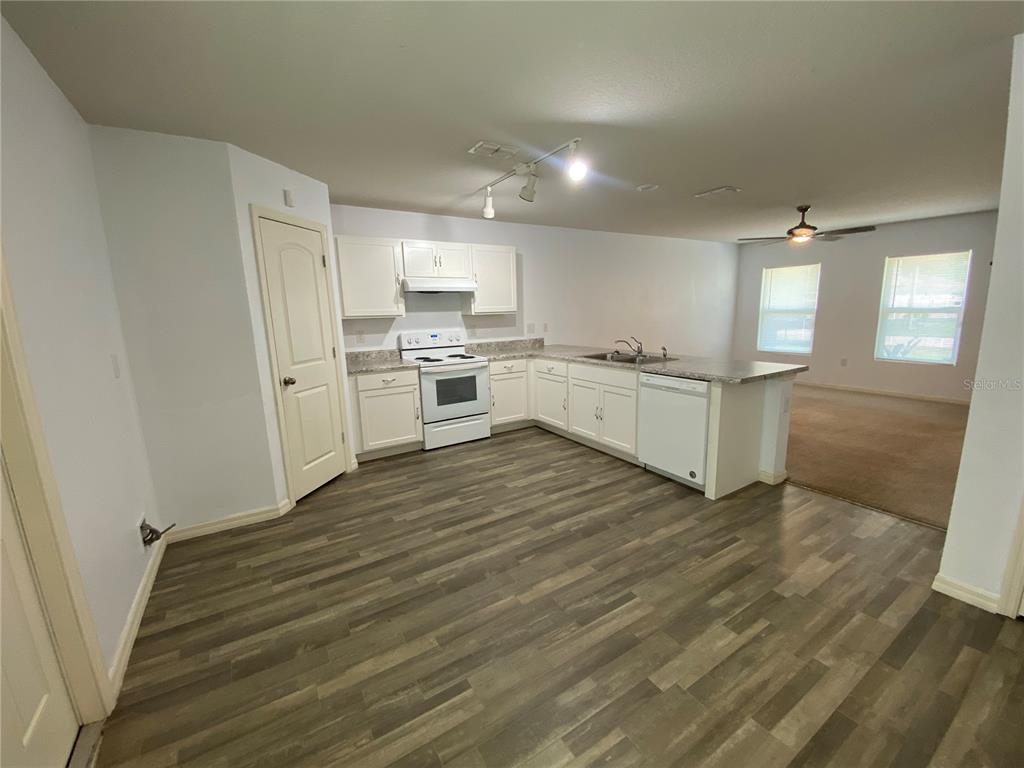 A kitchen with white cabinets, light countertops, and wood-look flooring opens to a carpeted area — 204 GLADIOLA COURT, KISSIMMEE, FL