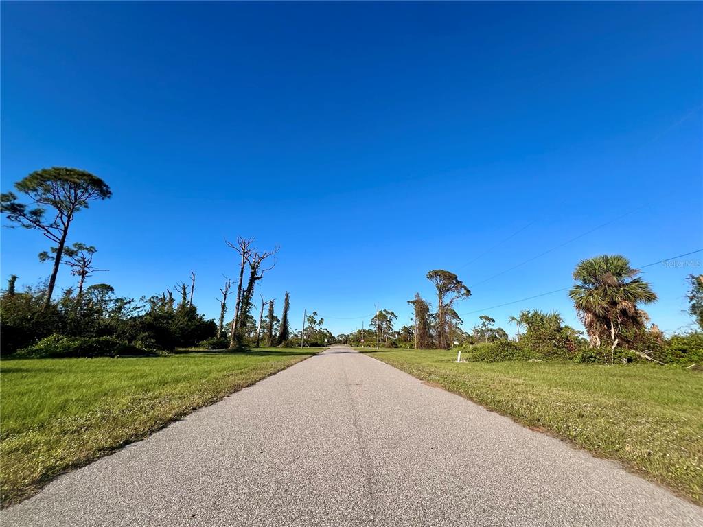 A paved road stretches through a grassy, undeveloped lot with scattered trees under a clear sky — 8 PENNANT PLACE, PLACIDA, FL