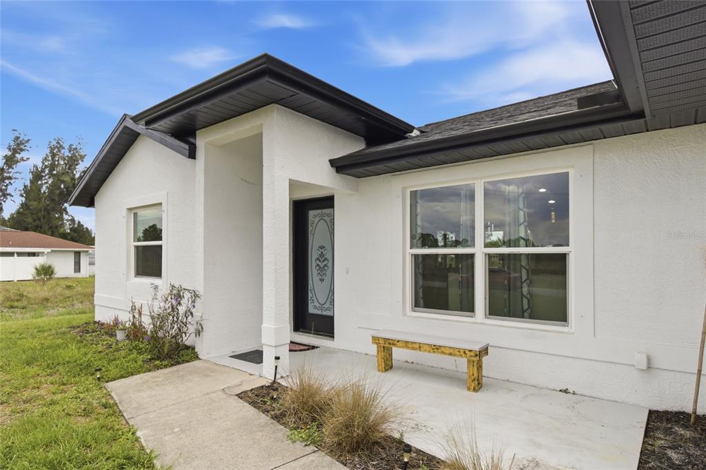 A white stucco house exterior features a dark front door, a bench, and a walkway — 12123 MALLORCA AVENUE, NORTH PORT, FL