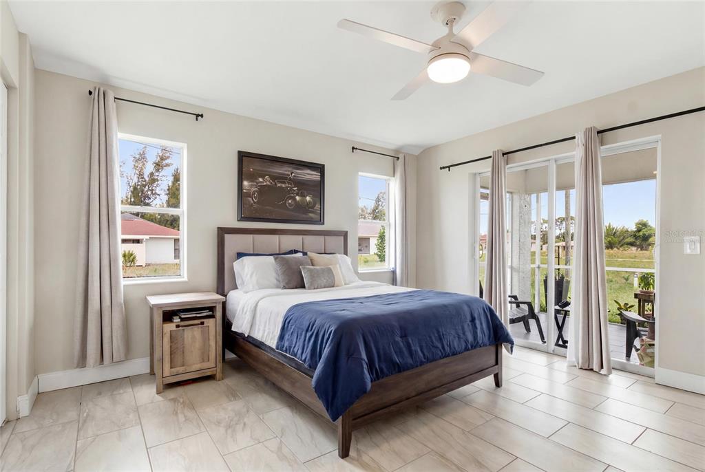 A bedroom features a bed, tile flooring, a ceiling fan, and sliding glass doors to a patio — 12123 MALLORCA AVENUE, NORTH PORT, FL