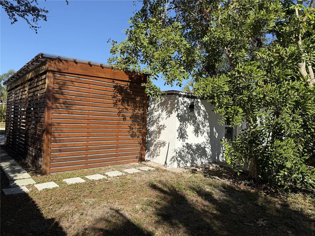 A wooden slatted structure stands next to a white stucco building in a grassy yard — 907 FRUITLAND AVENUE, BRADENTON, FL