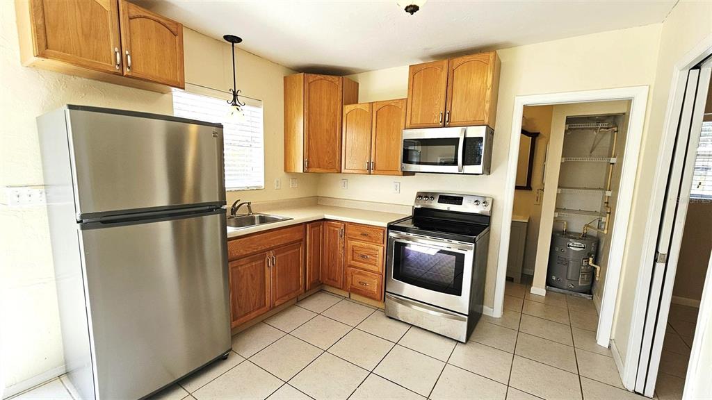 A kitchen features stainless steel appliances, wood cabinets, and light-colored tile flooring — 865 PALM AVENUE UNIT A, ENGLEWOOD, FL