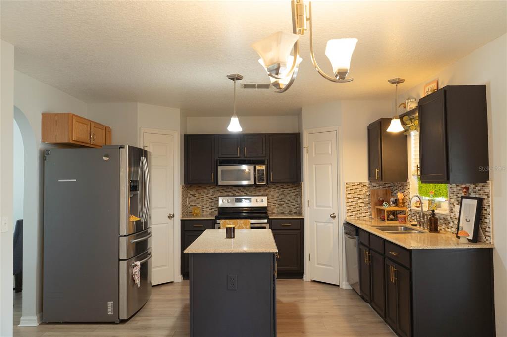 A kitchen features dark cabinetry, stainless steel appliances, a center island, and a tiled backsplash — 186 CEDAR RIDGE LANE, SANFORD, FL