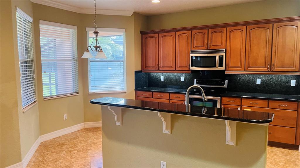 A kitchen features wood cabinets, black countertops, a breakfast bar, and a dining nook — 1221 DUMAINE AVENUE, PORT ORANGE, FL