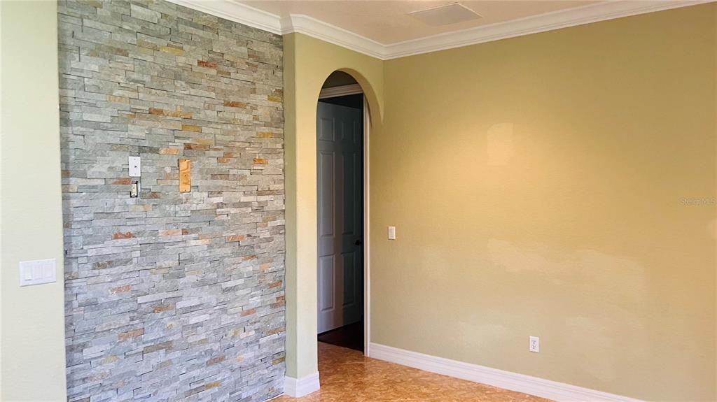 A room with a stone accent wall, a yellow wall, and an arched doorway — 1221 DUMAINE AVENUE, PORT ORANGE, FL