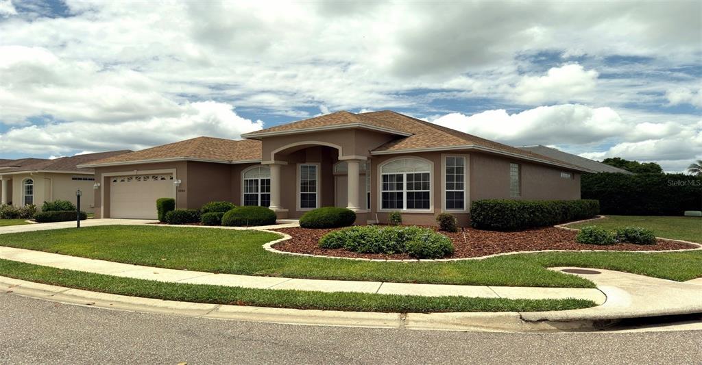 A single-story house with a tan stucco exterior, a brown shingled roof, and landscaped yard — 2805 HONEYWELL PLACE, LAKELAND, FL