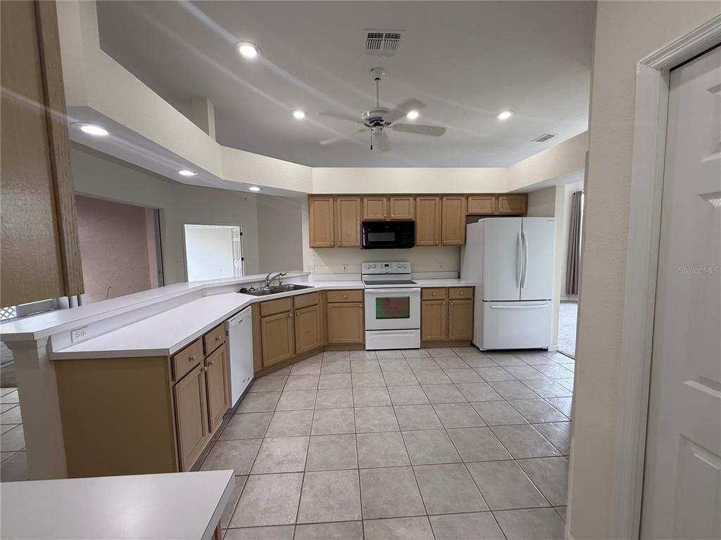 A kitchen with light wood cabinets, white appliances, white countertops, and beige tile flooring — 2805 HONEYWELL PLACE, LAKELAND, FL