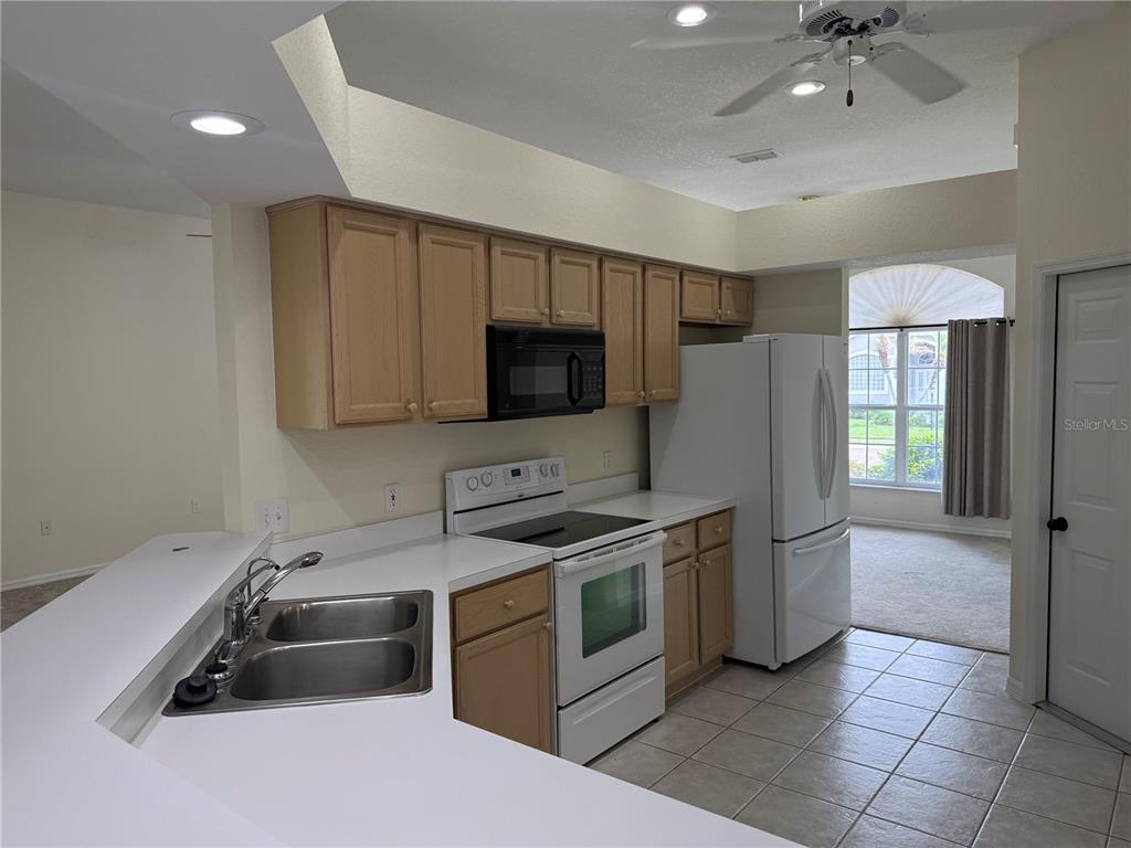 A kitchen features light wood cabinets, white appliances, white countertops, and tile flooring — 2805 HONEYWELL PLACE, LAKELAND, FL