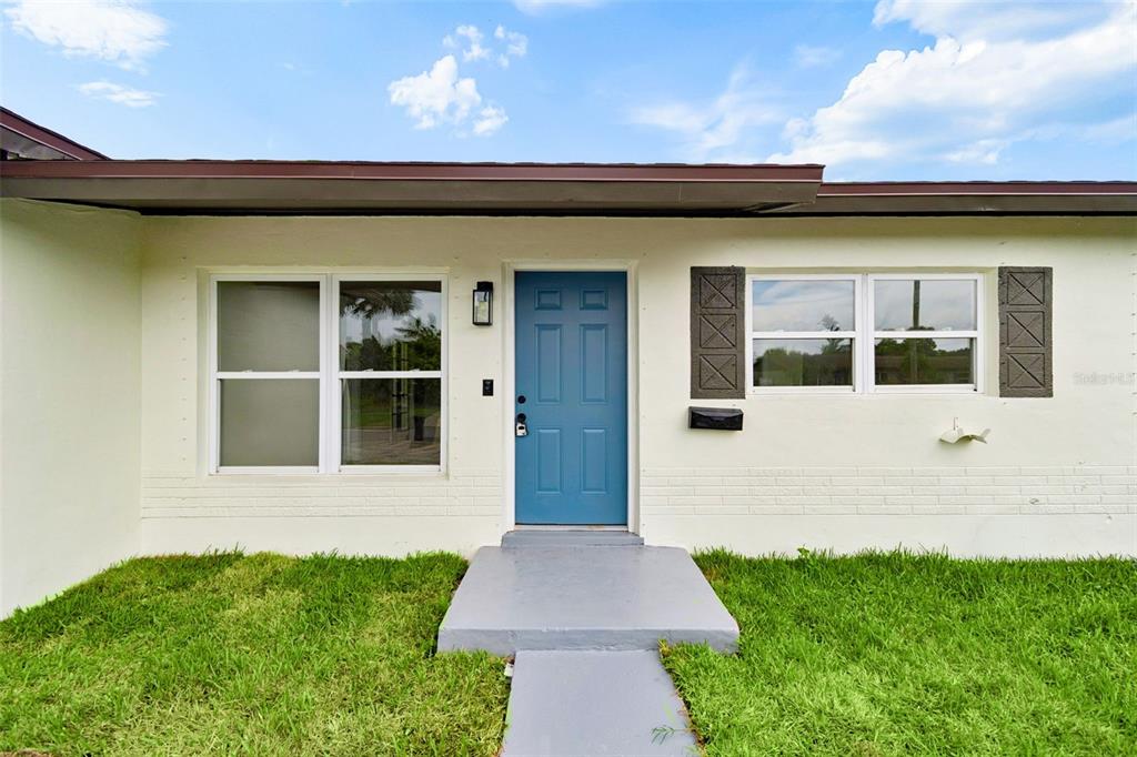The exterior of a house features a blue front door, white brick walls, and windows — 6781 33RD AVENUE N, ST PETERSBURG, FL