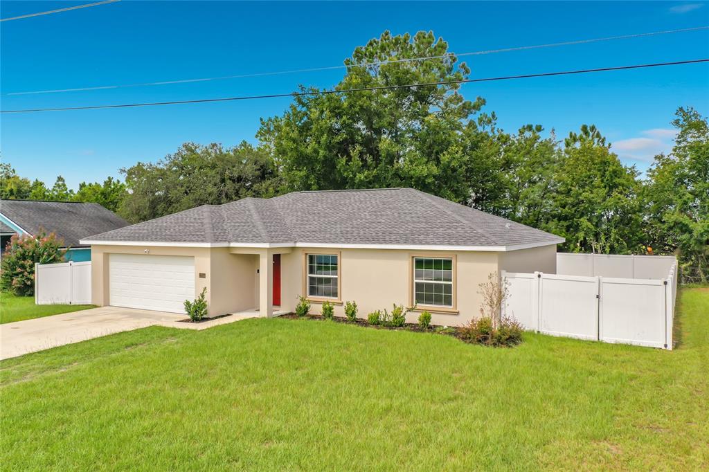 A single-story house with a beige stucco exterior, a two-car garage, and a white fence — 13244 49TH, OCALA, FL