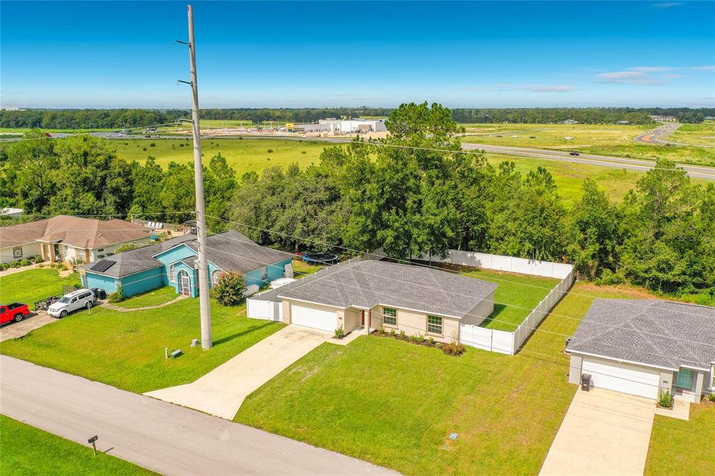 An aerial view shows three suburban houses with driveways and lawns near a grassy field — 13244 49TH, OCALA, FL