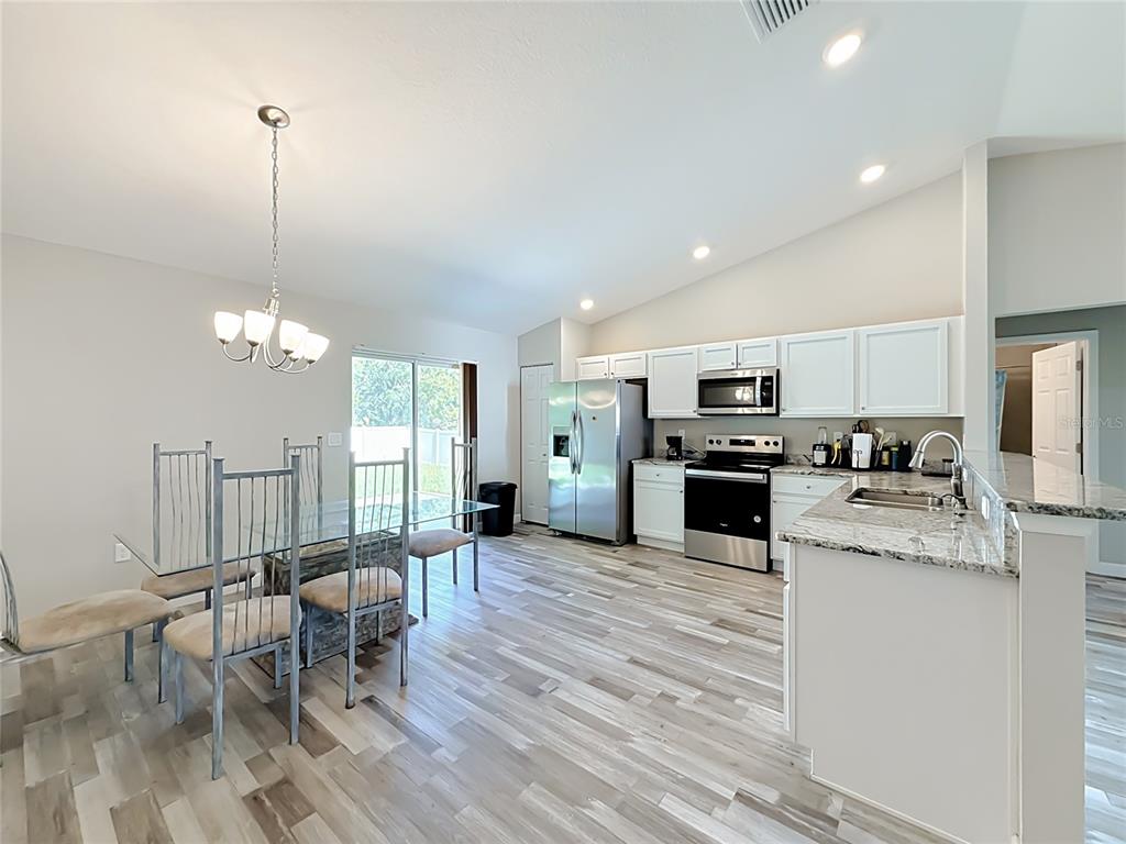 A kitchen and dining area feature white cabinets, stainless steel appliances, and light wood-look flooring — 13244 49TH, OCALA, FL