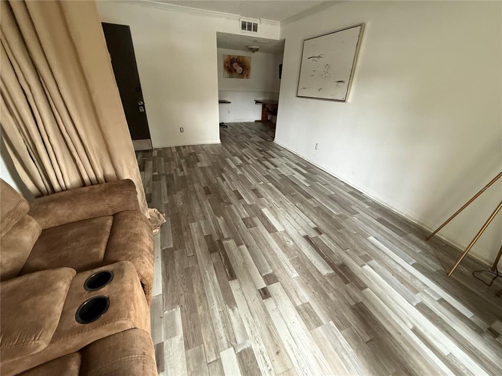 A living room with wood-look flooring, a brown sofa, and a view into an adjacent room — 305 WYMORE ROAD UNIT 100, ALTAMONTE SPRINGS, FL