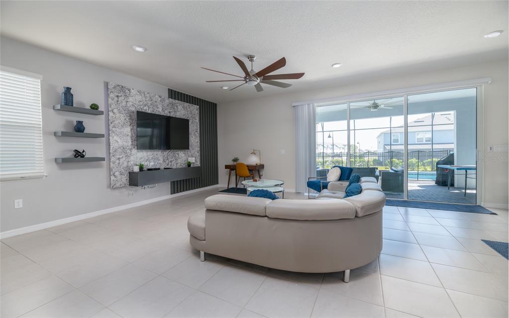 A living room features a curved sofa, a marble-accented media wall, and sliding glass doors — 3217 LILAC WAY, DAVENPORT, FL