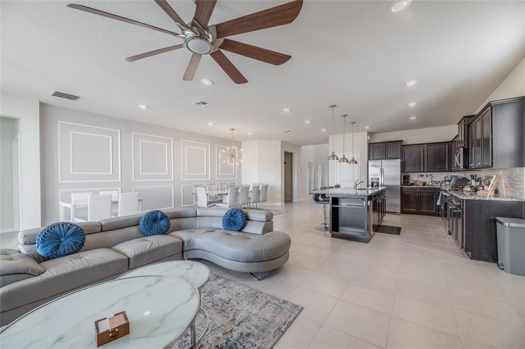 An open-concept living room and kitchen feature a grey sectional, dining area, and dark cabinetry — 3217 LILAC WAY, DAVENPORT, FL